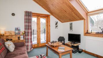 Una sala de estar acogedora con techo de madera, chimenea, televisor y sofá.