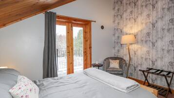 Ein Schlafzimmer mit Holzbalkendecke, einem Bett mit weißer Decke, einem Sessel mit Blumenkissen, einem kleinen Tisch und einer Lampe.