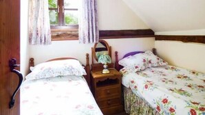 A bedroom with two single beds, a wooden dresser, a mirror, and a window with curtains. - The Granary (Norwich)