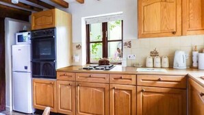 A kitchen with wooden cabinets, a built-in oven, and a window with a view of greenery. - The Granary (Norwich)