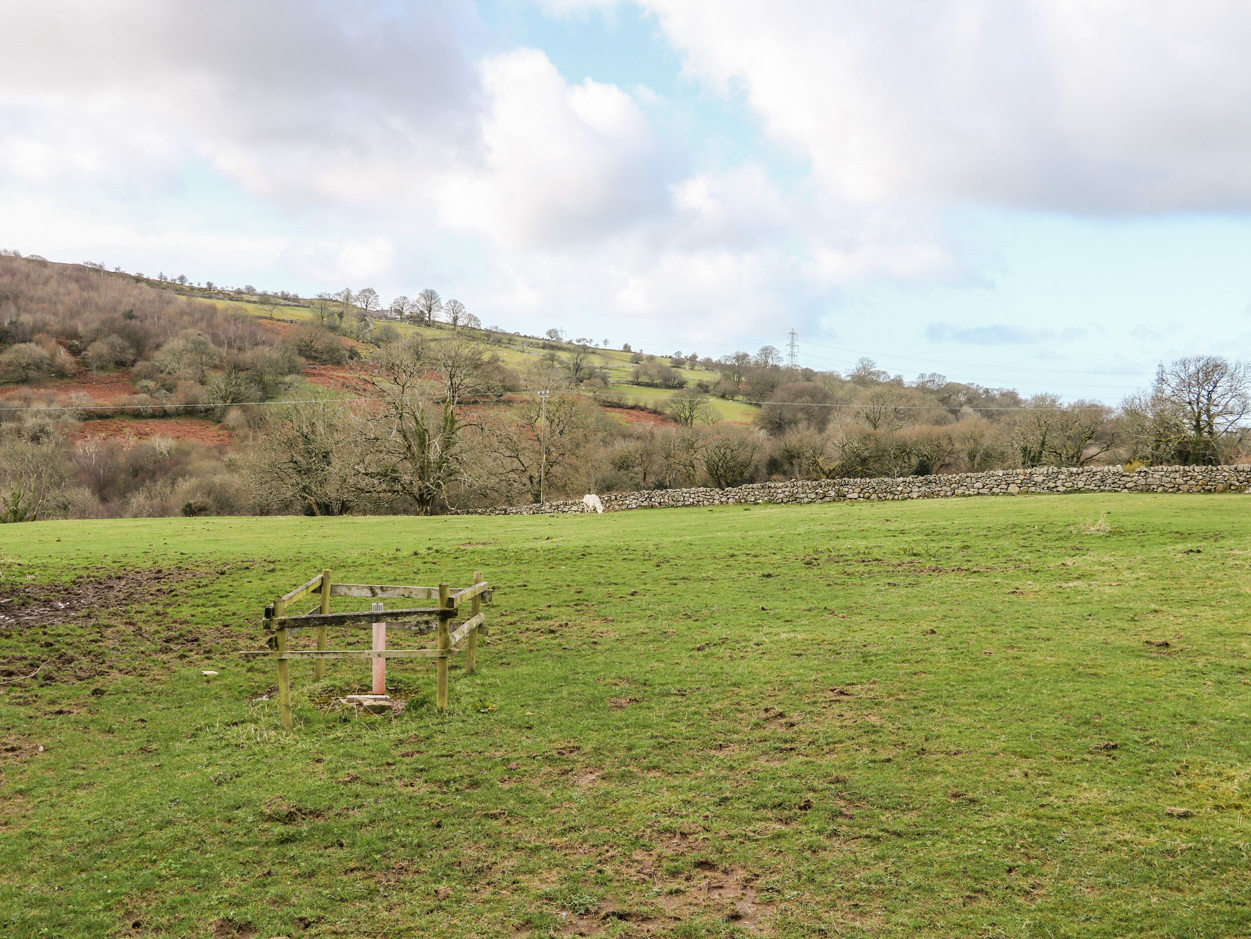 A rural landscape with a stone wall, a wooden fence, and a grassy field.