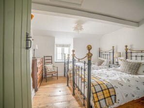 A bedroom with a wooden floor, a bed with a metal frame, a chair, a dresser, and a window. - Bwthyn Dyfi (Machynlleth)