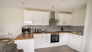 A modern kitchen with white cabinets, a microwave, an oven, and a coffee maker. - Beechnut Cottage (Tewkesbury)