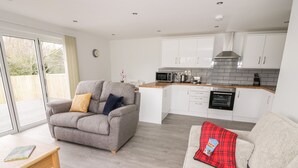 A modern kitchen with white cabinets and a grey sofa with a red plaid throw. - Beechnut Cottage (Tewkesbury)