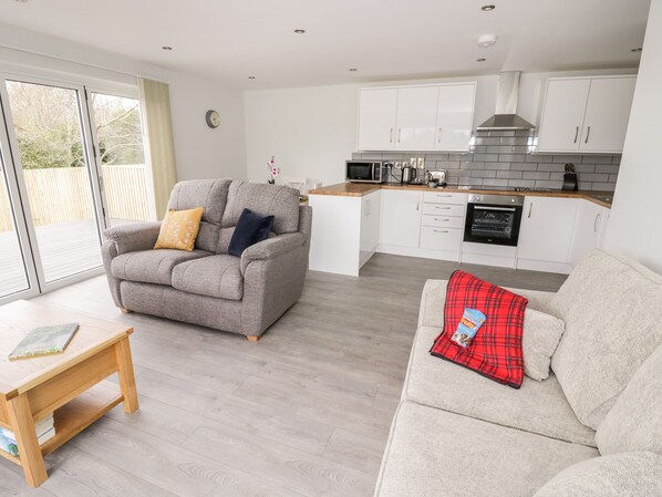 A modern kitchen with white cabinets and a grey sofa with a red plaid throw.