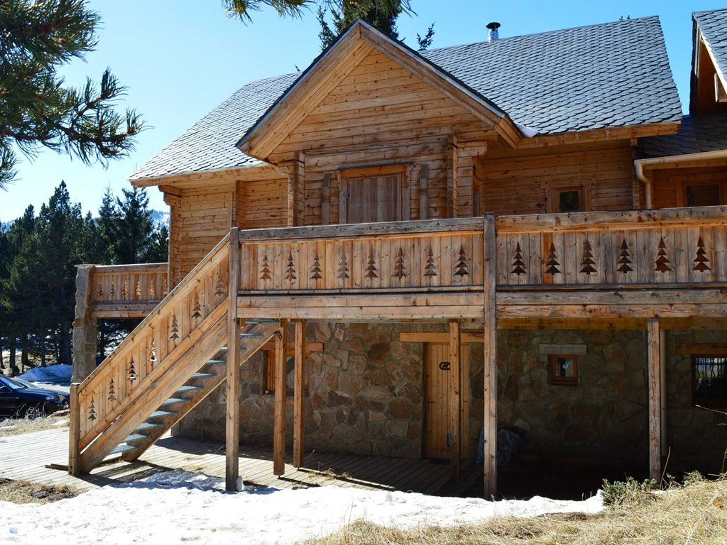 A wooden cabin with a stone foundation, a wooden staircase, and a balcony with a railing.