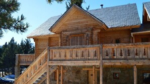 A wooden cabin with a stone foundation, a wooden staircase, and a balcony with a railing.