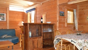 A wooden cabin interior with a sofa, a dining table with chairs, a wooden cabinet, and a window.