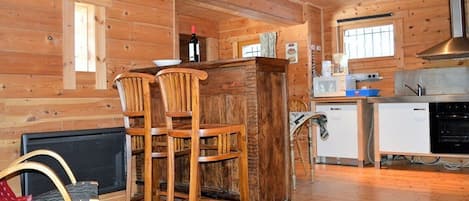 A wooden cabin interior with a kitchen area, a dining table, and two wooden chairs.