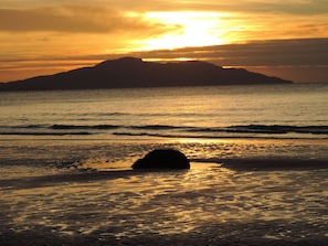 Una spiaggia con una roccia in primo piano e la sagoma di una montagna sullo sfondo.