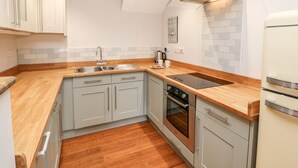 Eine kleine Küche mit grauen Schränken, einer Holz Arbeitsplatte, einer Edelstahl-Spüle, einem eingebauten Backofen und einer modernen Dunstabzugshaube.