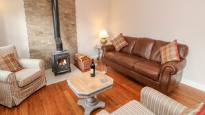 Ein gemütliches Wohnzimmer mit einer Steinwand, einem braunen Ledersofa, gestreiften Sesseln, einem Holztisch und einem Kaminofen.