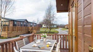 Une terrasse en bois avec une table dressée pour le repas, donnant sur un quartier résidentiel avec des maisons et une route.