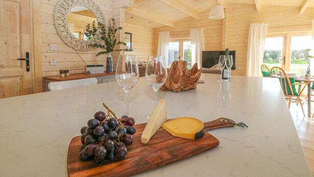 A wooden cabin interior with a marble dining table, a wooden cutting board with grapes and cheese, and a wooden bowl.