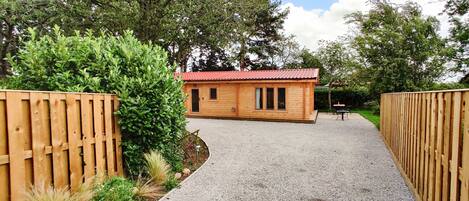 A wooden cabin with a red roof, surrounded by a gravel path and wooden fences.