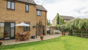 A two-story brick house with a patio area featuring a table and chairs, a white umbrella, and potted plants. - Kite Cottage (Brackley)