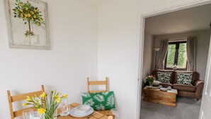A dining area with a wooden table set for four, a sofa in the background, and a painting on the wall. - Kite Cottage (Brackley)