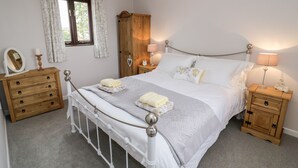 A neatly arranged bedroom with a bed, wooden nightstands, a dresser, and a window with curtains. - Kite Cottage (Brackley)