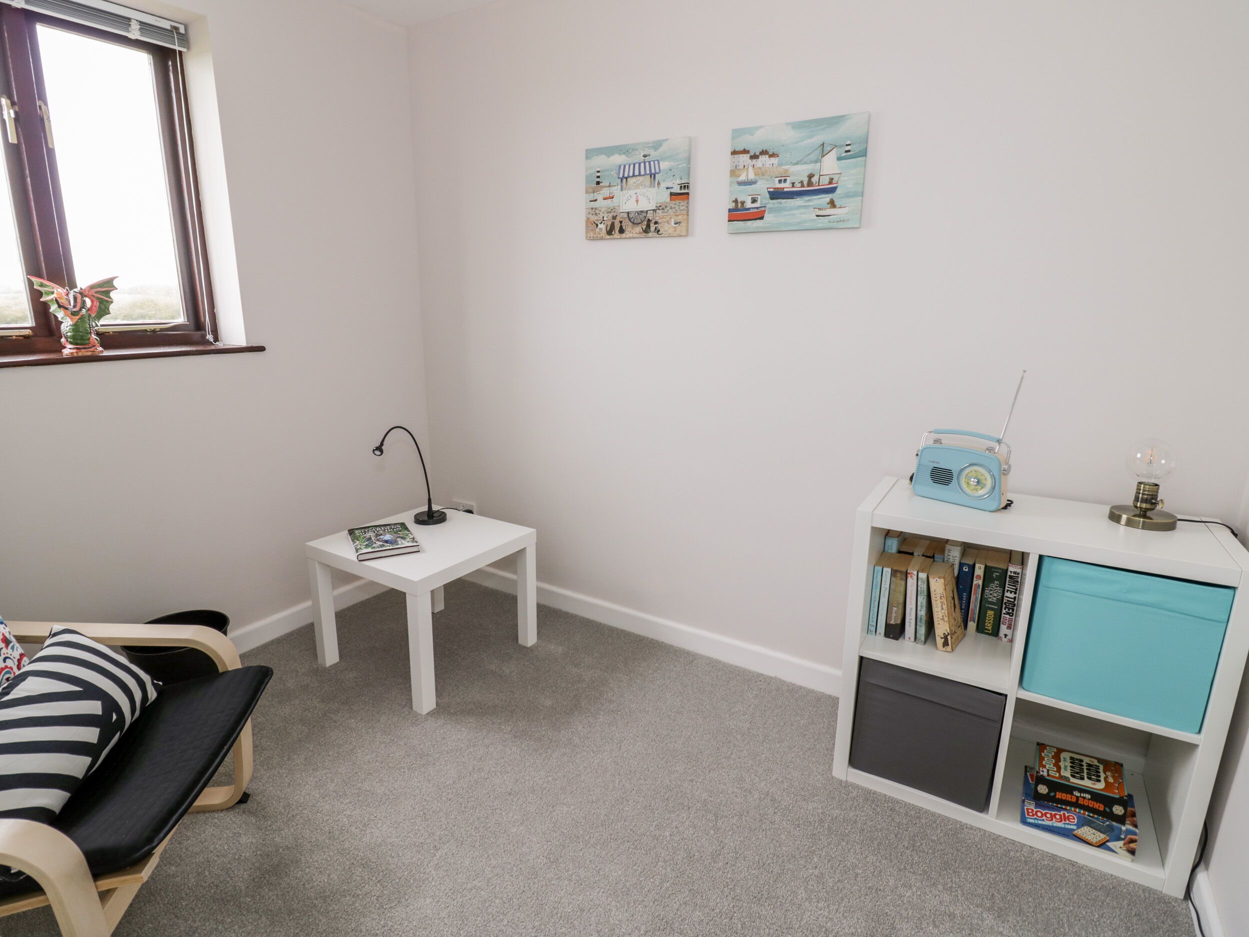 A child's playroom with a white desk, a small table, a bookshelf, and a window with curtains.