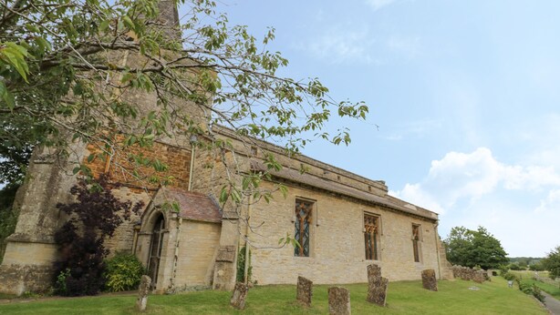 A historic stone church with a tall steeple, arched windows, and a grassy lawn. - Kite Cottage (Brackley)