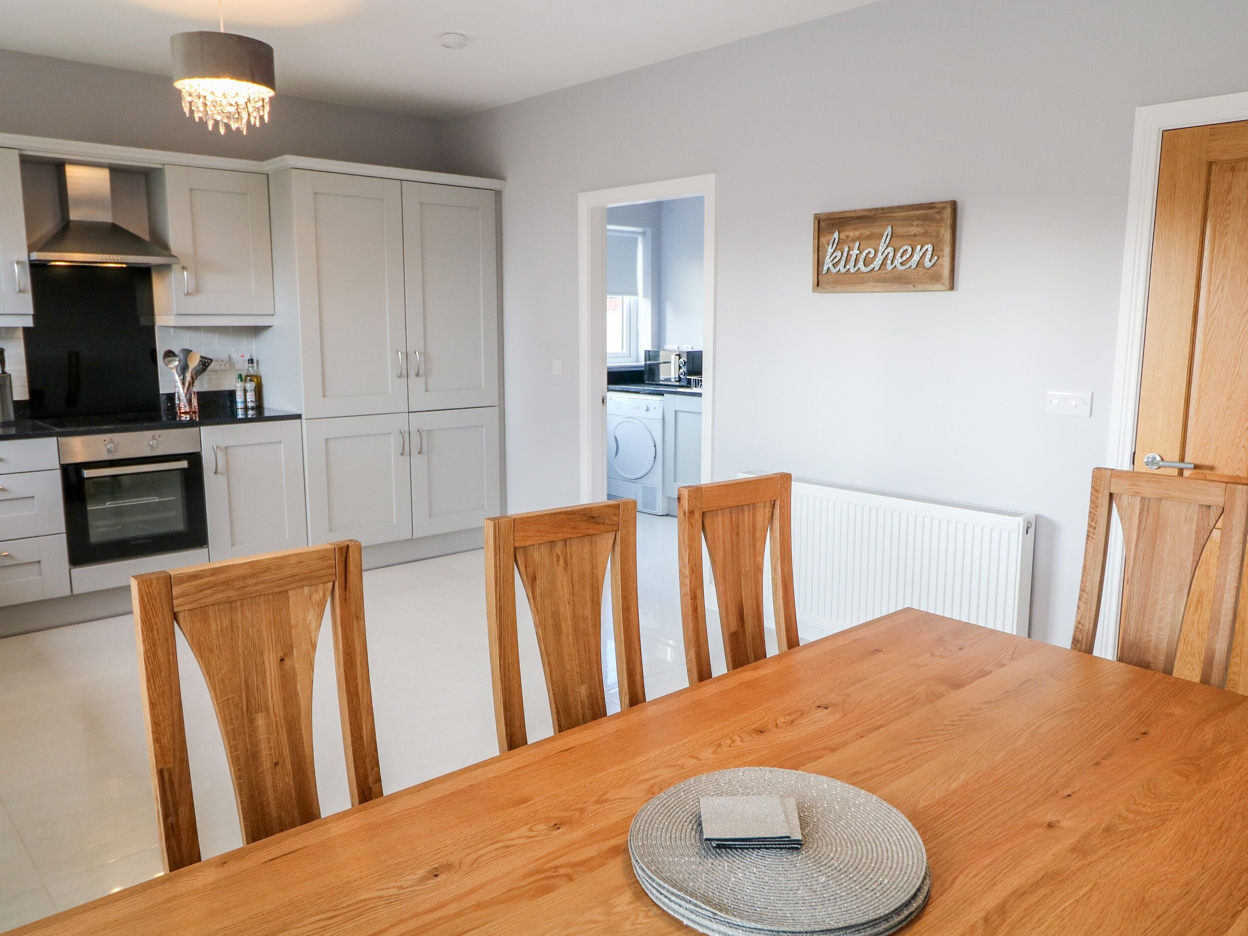 Una cocina moderna con armarios blancos, una mesa de comedor con sillas de madera y un cartel de cocina.