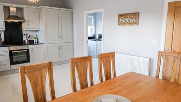 Una cocina moderna con armarios blancos, una mesa de comedor con sillas de madera y un cartel de cocina.