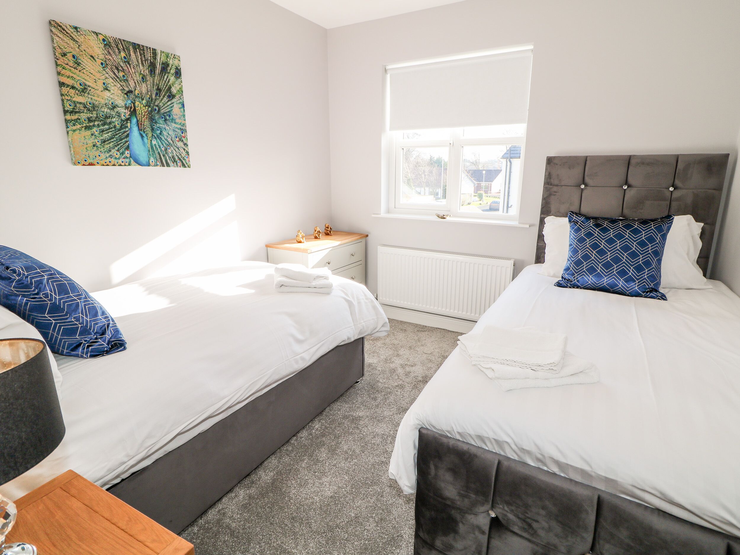 A bedroom with two beds, a nightstand, a window with blinds, and a painting on the wall.