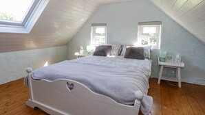 Une chambre avec un plafond en pente, un lit doté d’une tête de lit en forme de cœur, deux tables de chevet avec des lampes et une fenêtre laissant entrer la lumière naturelle.