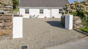 Une maison blanche avec une allée en gravier, des murs en pierre et un jardin fleuri.