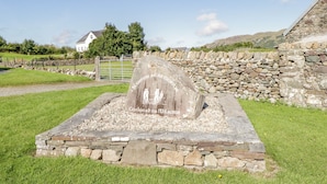 Un monument de pierre orné d’inscriptions, entouré d’un mur de pierre et d’une zone herbeuse.