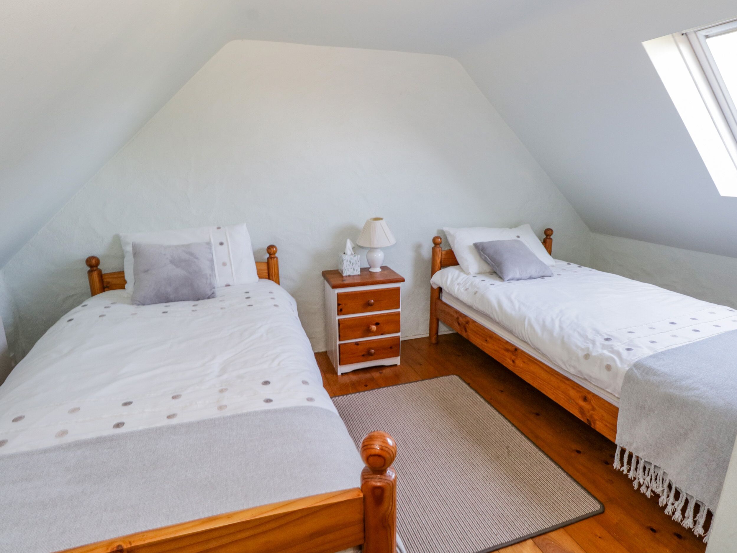 A small, well-lit attic bedroom with two wooden beds, a nightstand, and a window.
