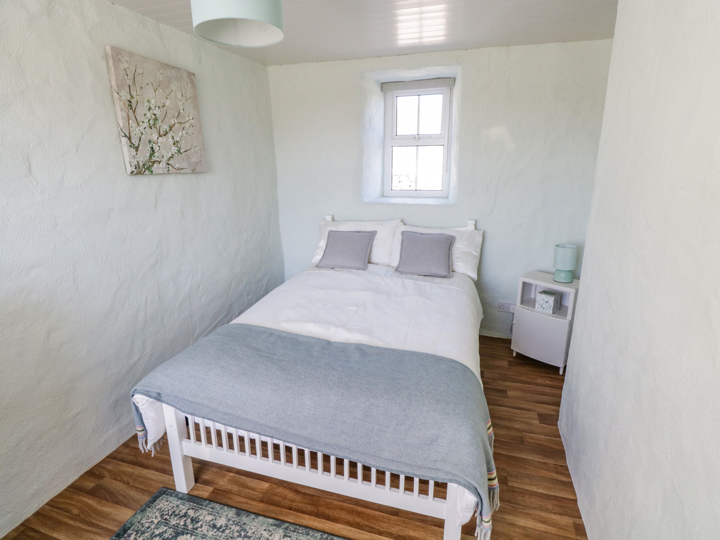 A bedroom with a bed, a nightstand, a lamp, a window, and a painting on the wall.