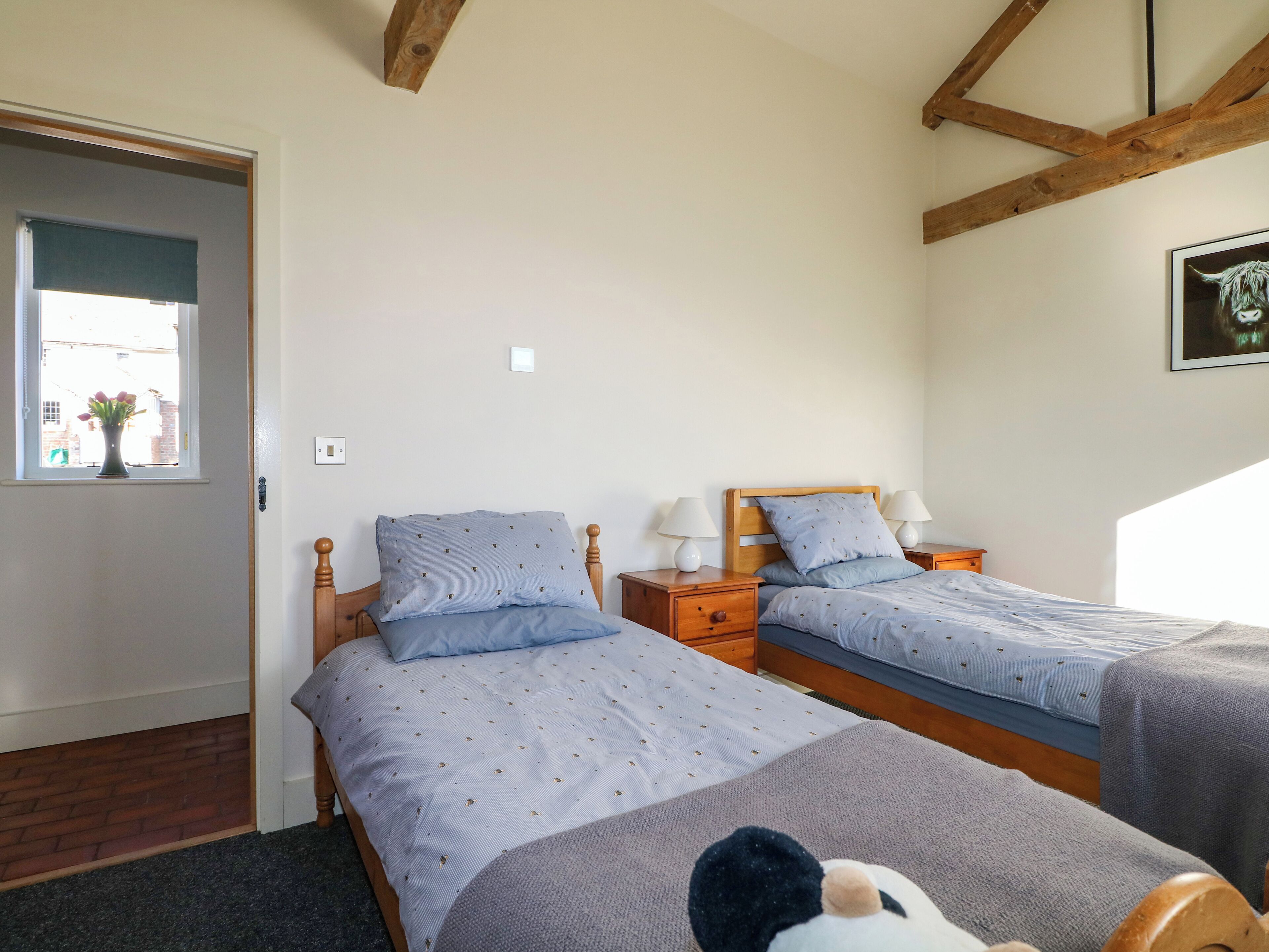 Un dormitorio con dos camas individuales, cabeceros de madera, mesitas de noche con lámparas, una ventana con vistas y una puerta.
