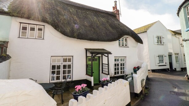 A white building with a thatched roof, a green door, and multiple windows. - Teign Cottage (Teignmouth)