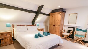 A bedroom with a large bed, wooden wardrobe, two nightstands, a desk, and a chair. - Teign Cottage (Teignmouth)