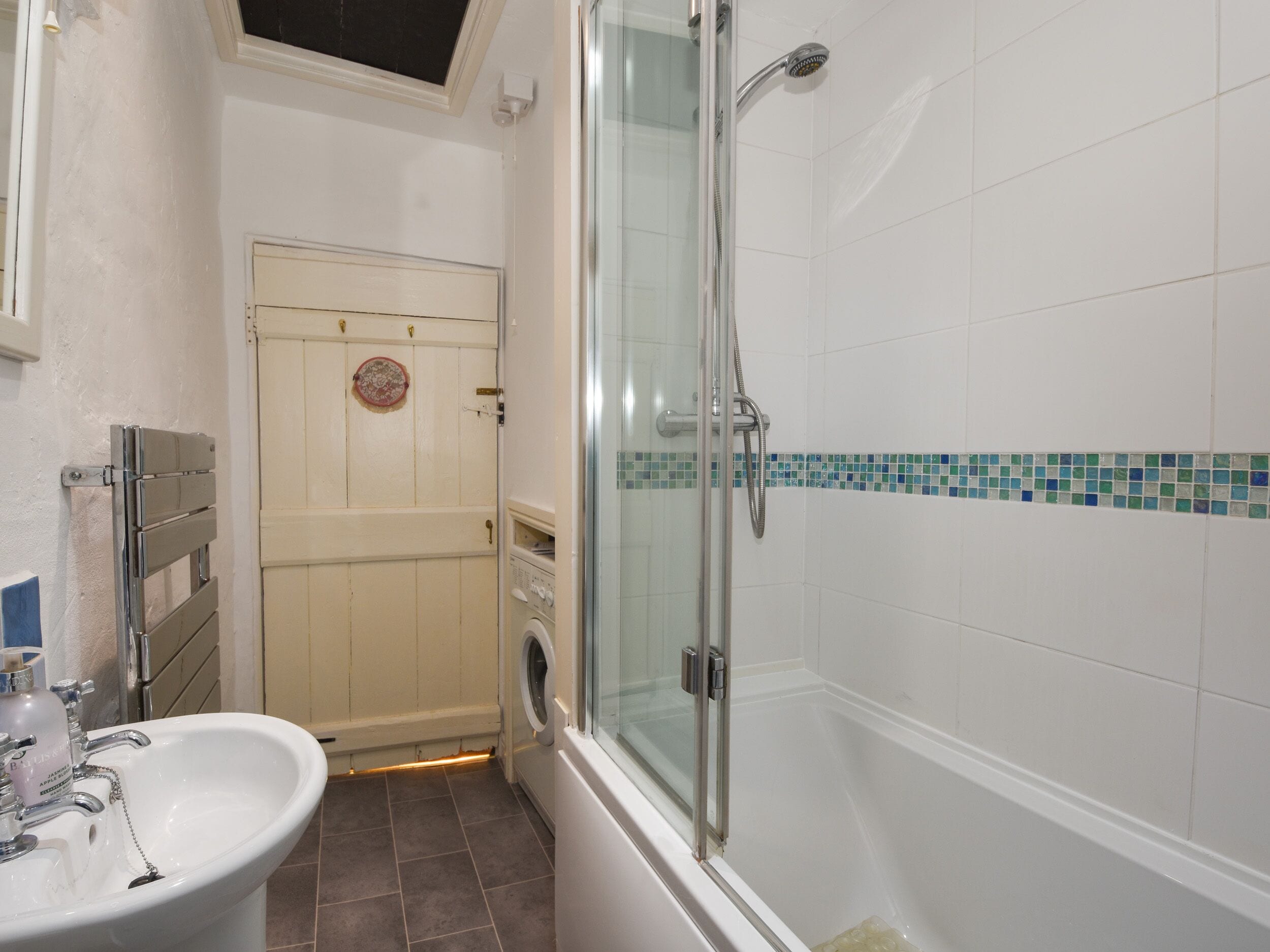Un baño con cabina de ducha de vidrio, lavamanos y lavadora.