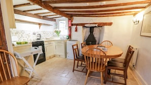 A rustic kitchen with a wooden table and chairs, a stove, and a sign that says "WELCOME". - Teign Cottage (Teignmouth)