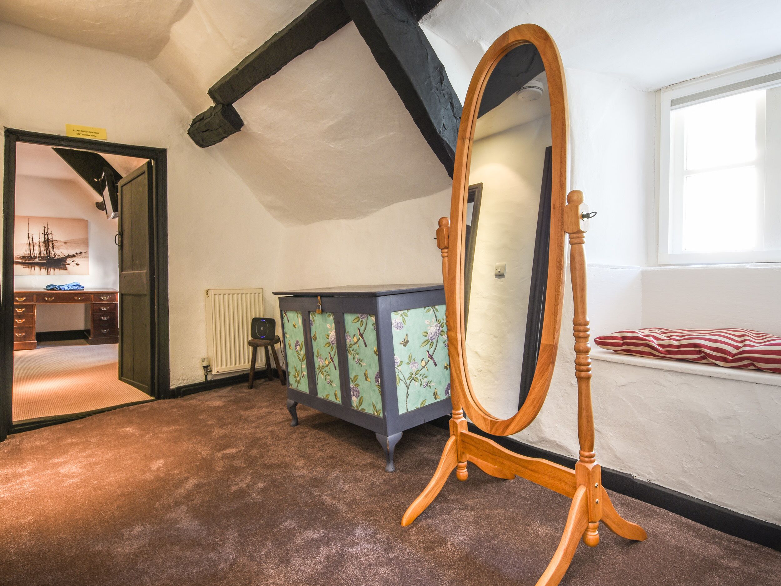 A room with a wooden-framed mirror, a radiator, a desk with drawers, and a window with a view.