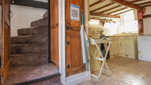 A staircase leading to a kitchen with wooden beams, a whiteboard, and a QR code on the door. - Teign Cottage (Teignmouth)