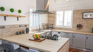 A modern kitchen with a central island, bar stools, a built-in washing machine, and a brick accent wall. - Bay View (Holyhead)