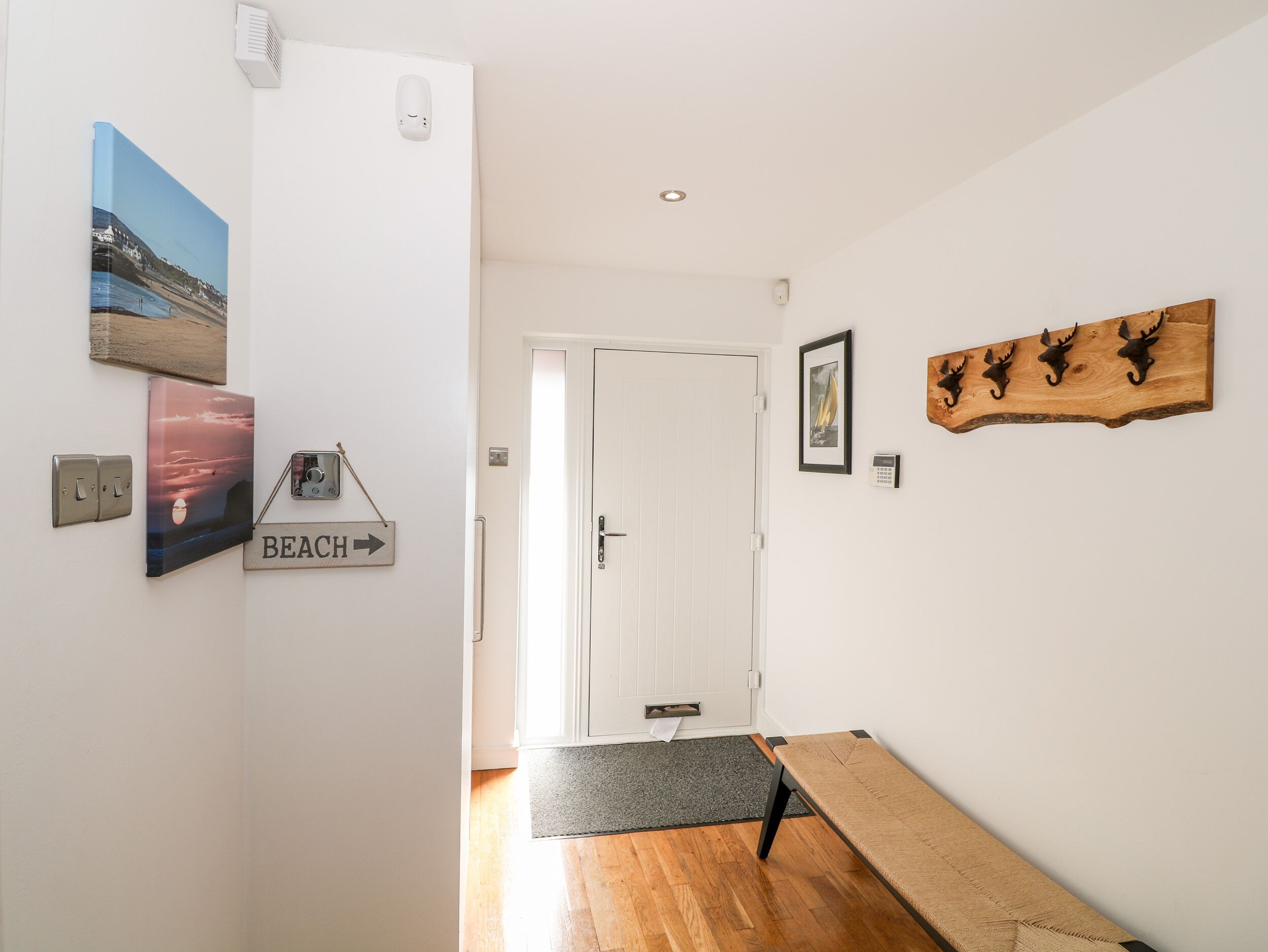 Un corridoio con una panca di legno, una porta e opere d'arte appese al muro, tra cui un segnale con la scritta 'BEACH'.