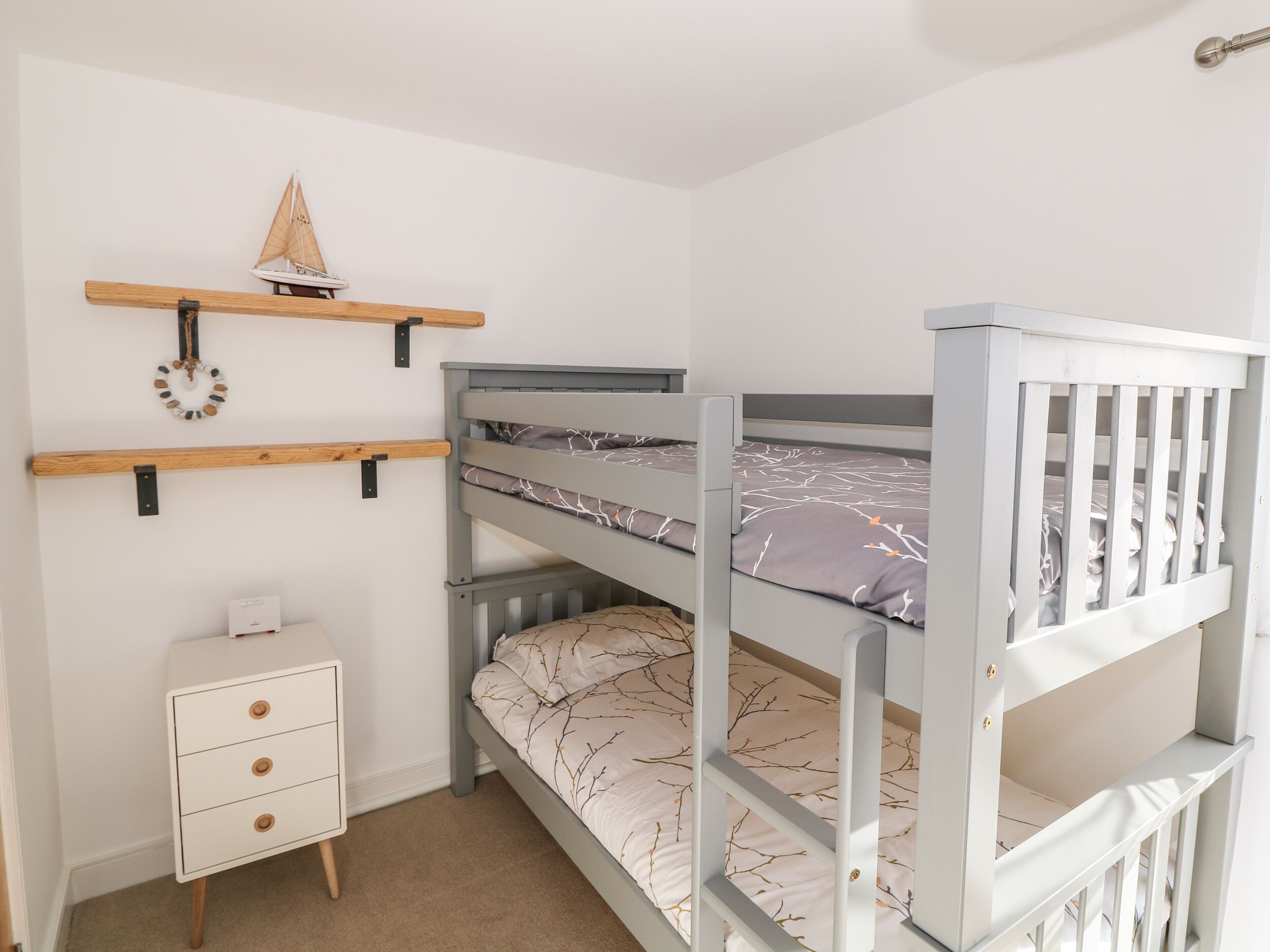 A bunk bed with a desk and drawers, a small shelf with a model ship, and a wall-mounted decoration.