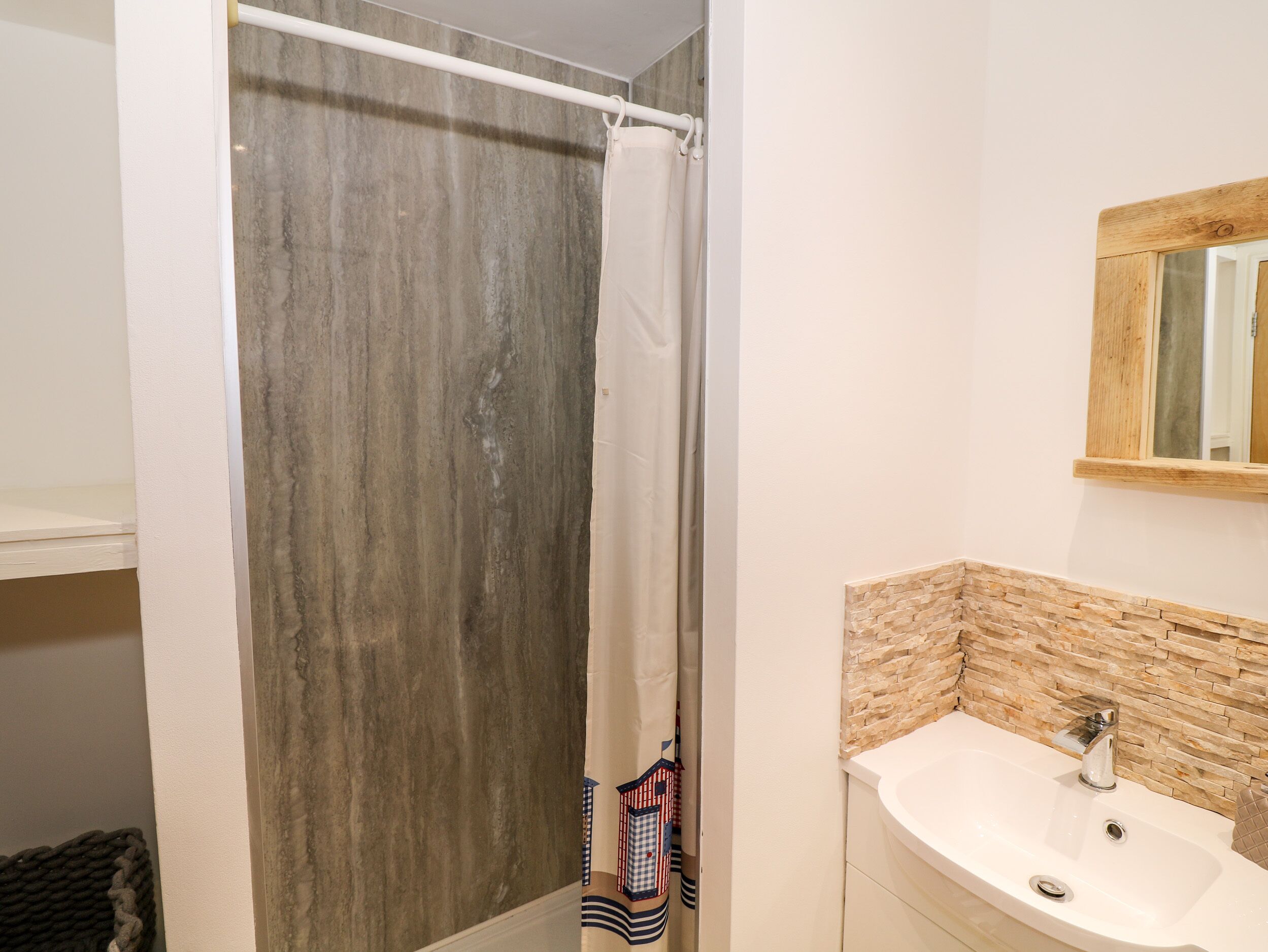 A bathroom with a shower curtain, a sink with a stone backsplash, and a mirror above the sink.