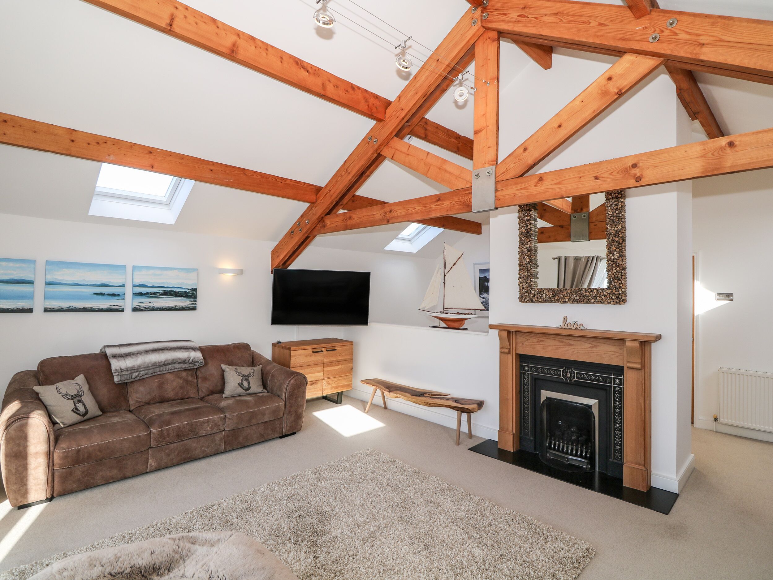 A spacious living room with a high ceiling, wooden beams, a fireplace, a television, and a cozy sofa.