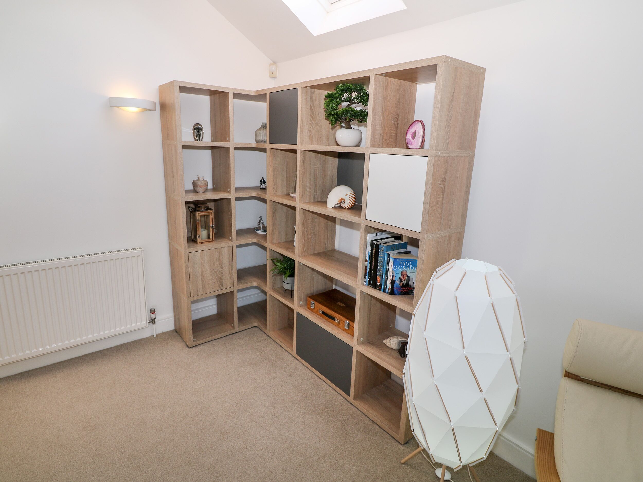 A room with a built-in wooden bookshelf, a radiator, and a white chair.