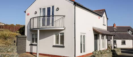 A two-story house with a balcony, stone wall, and a clear sky.