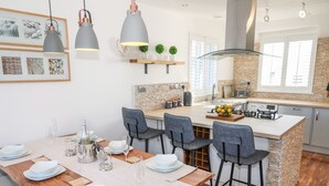 A modern kitchen with a central island, bar stools, and pendant lighting. - Bay View (Holyhead)