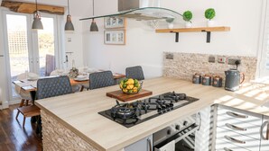 A modern kitchen with a central island, built-in oven, and a dining area with chairs and a table. - Bay View (Holyhead)