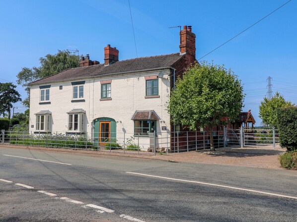 A two-story white building with a green door and windows, a brick chimney, and a fenced garden area. - Bellamour End Cottage (Rugeley)