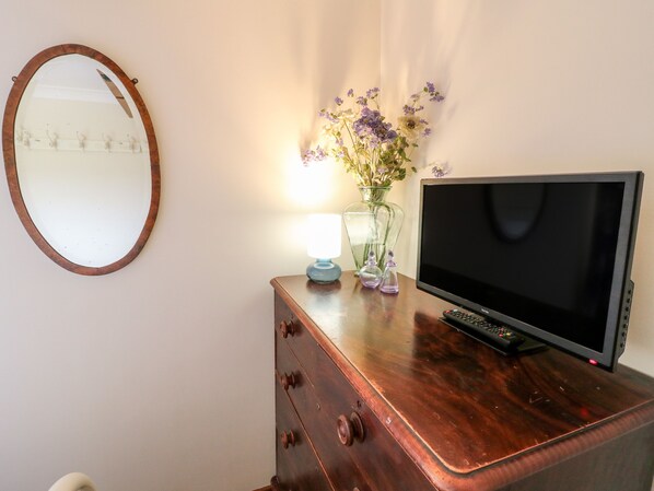 A wooden dresser with a television, a mirror, and a vase with flowers. - Bellamour End Cottage (Rugeley)